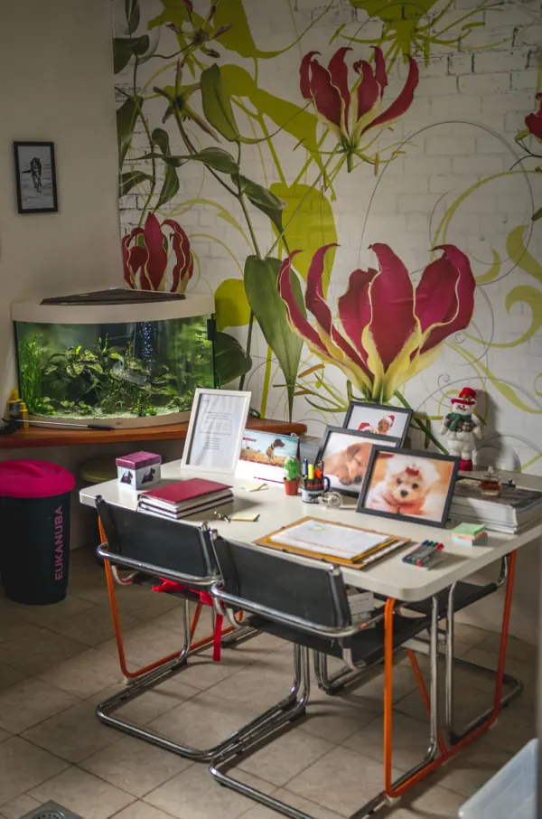 Recepcija hotela sa stolom, akvarijem i cvjetnim zidnim oslikom, na stolu uokvirene fotografije pasa.